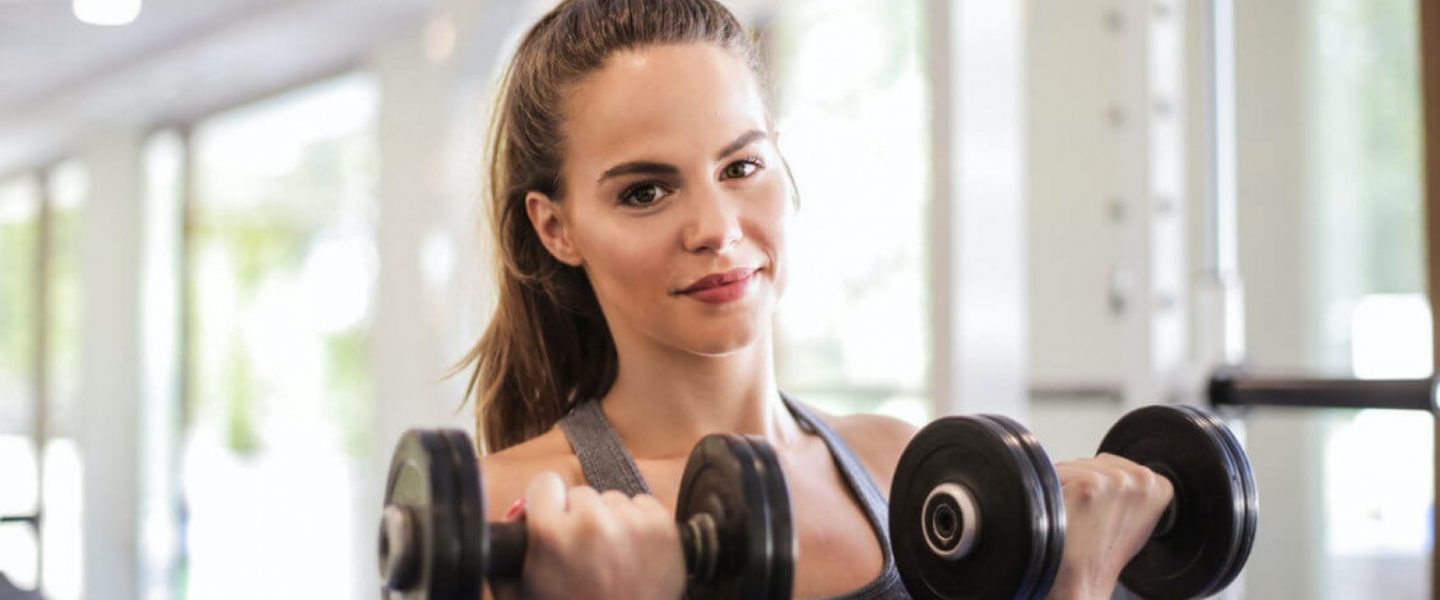 woman in gray tank top holding two black dumbbells 3757370 1536x775 1
